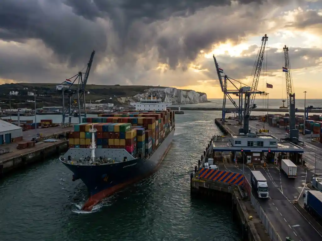 Groot containerschip vaart door smal kanaal bij witte kliffen van Dover met douanecontrolepost en havenkranen